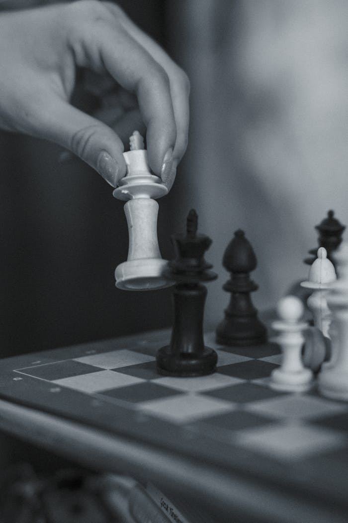 A close-up of a strategic chess move with a human hand on a wooden chessboard.