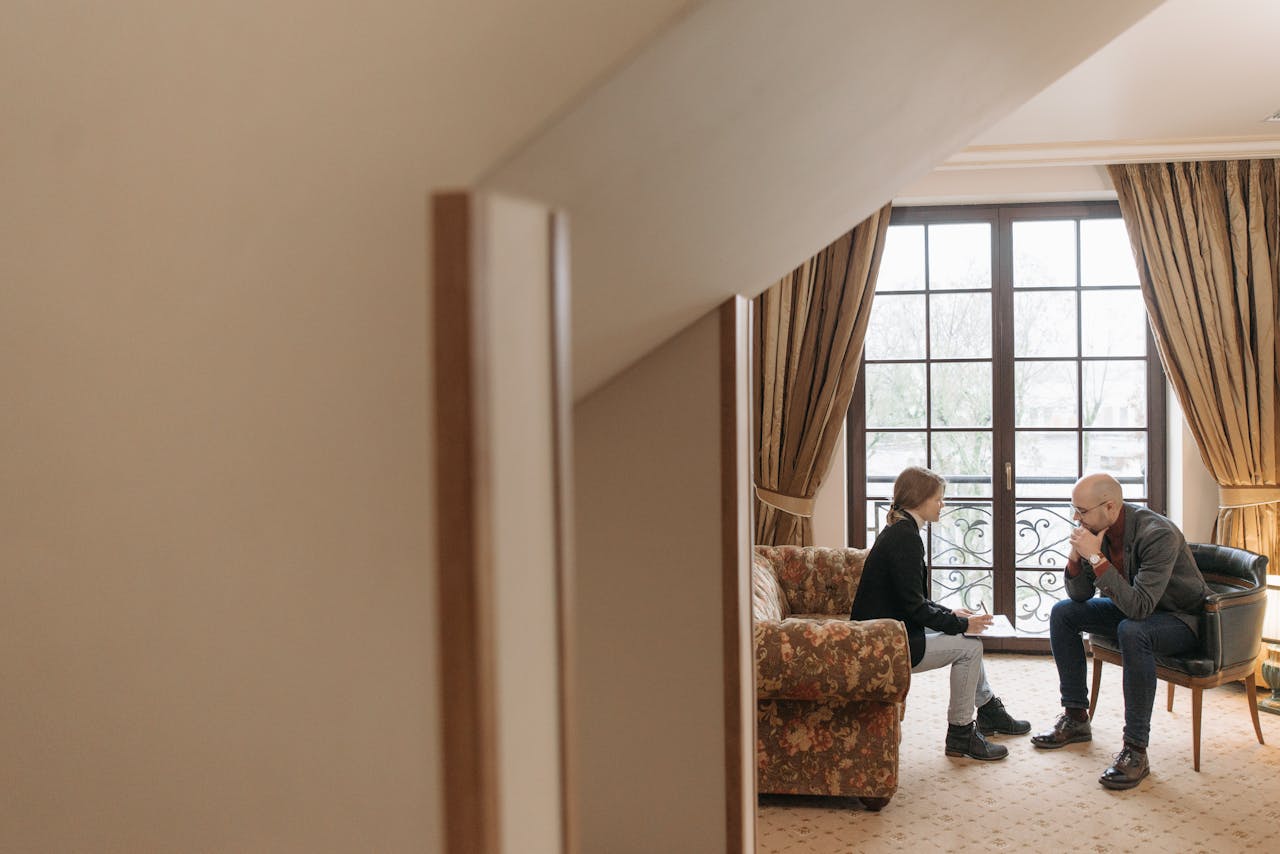 Two professionals in a serious discussion in a tastefully decorated office, featuring cozy furniture and large windows.